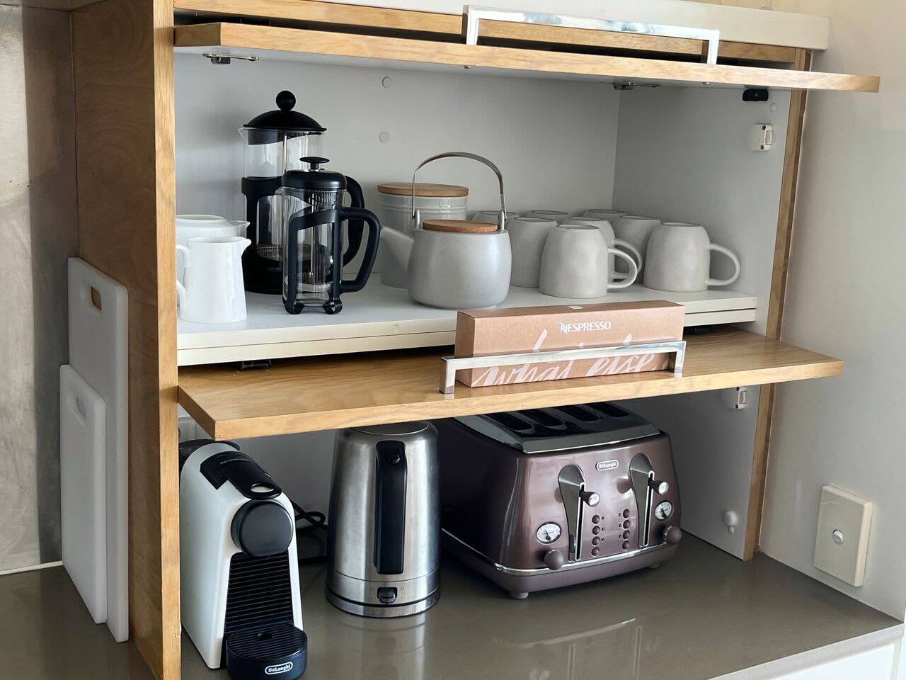 Una cocina con cafetera, hervidor, tostadora y una caja de cápsulas Nespresso.