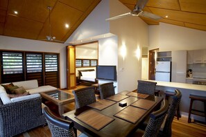 A modern living room with a dining area, a TV, and a kitchen. - Pure Magnetic Villa 3 (Nelly Bay)