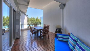 A balcony with a wooden floor, a table with chairs, a grill, and a blue sofa with striped cushions. - Maggies Beachfront Apt. 6 (Horseshoe Bay)