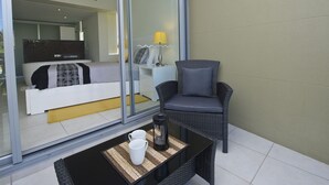 A modern room with a glass partition, a wicker chair, a small table with a coffee pot, and a bed with patterned bedding. - Blue on Blue Apartment 921 (Nelly Bay)