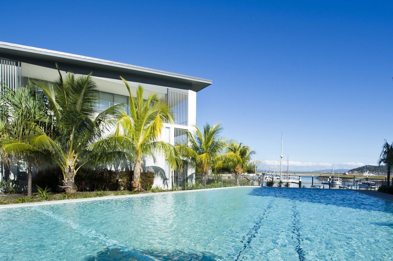 A modern hotel with a pool, palm trees, and a marina view.