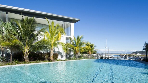 A modern hotel with a pool, palm trees, and a marina view. - Blue on Blue Apartment 921 (Nelly Bay)