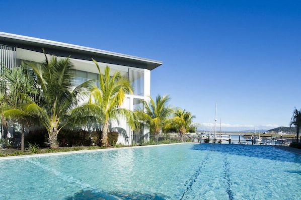 Ein modernes Hotel mit Pool, Palmen und Blick auf eine Marina.