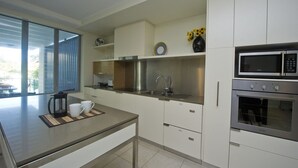 A modern kitchen with a stainless steel sink, a microwave, and an oven. - Blue on Blue Apartment 921 (Nelly Bay)