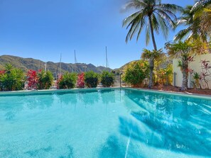 Ein klares, blaues Schwimmbecken, umgeben von tropischen Pflanzen und Palmen, mit Bergen im Hintergrund.