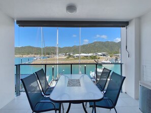 Ein Balkon mit Tisch und Stühlen, der auf einen Yachthafen mit Booten und Häusern blickt.