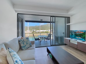 A modern living room with a sofa, coffee table, TV, and a balcony with a table and chairs. - Blue on Blue Superior Studio Room 1241 (Nelly Bay)
