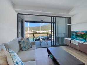 Ein modernes Wohnzimmer mit Sofa, Couchtisch, Fernseher und einem Balkon mit Tisch und Stühlen.