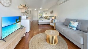 Un salon moderne doté d’un téléviseur à écran plat, d’un canapé gris, d’une table basse ronde et d’un ventilateur de plafond.