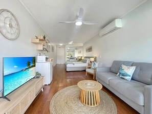 A modern living room with a flat-screen TV, a grey sofa, a round coffee table, and a ceiling fan. - Blue on Blue Studio Room 1222 (Nelly Bay)