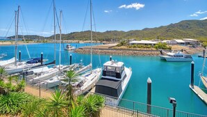 Un port de plaisance avec des bateaux amarrés, un ciel bleu dégagé et un paysage vallonné en arrière-plan.