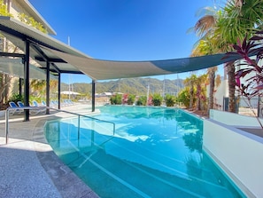 A swimming pool with clear water, surrounded by lounge chairs and palm trees.