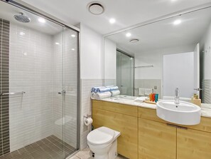 A modern bathroom with a glass shower enclosure, a white toilet, a wooden vanity with a sink, and a large mirror.