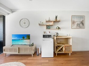 A living room with a television, a white refrigerator, wooden shelves with decorative items, and a framed picture on the wall. - Blue on Blue Studio Room 1222 (Nelly Bay)