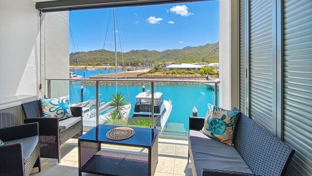 Un balcon avec vue sur un port de plaisance, une piscine et des collines.