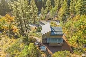 A two-story cabin with a deck and hot tub, surrounded by dense forest.