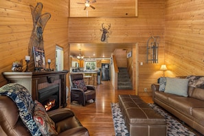 A cozy cabin interior with a fireplace, leather furniture, a dining area, and a kitchen.