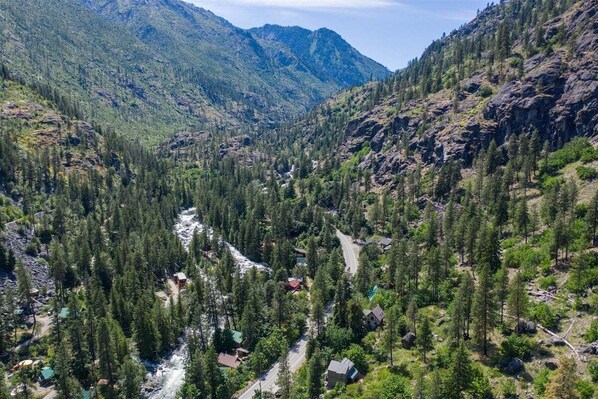 Un paisaje montañoso con un río, bosque denso y edificios dispersos.