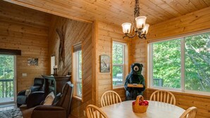 A wooden cabin interior with a dining table, chairs, a fireplace, and a bear statue.