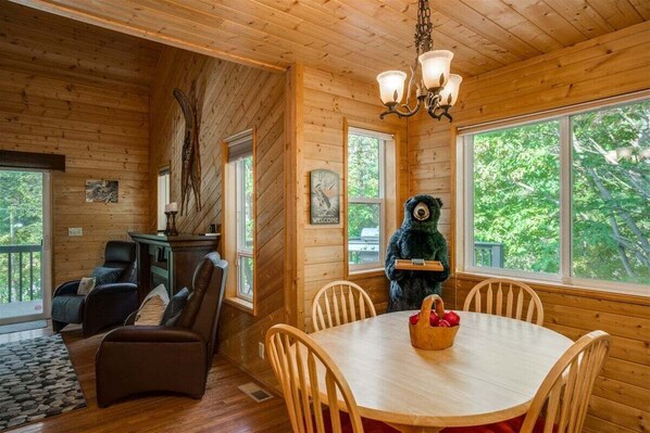 A wooden cabin interior with a dining table, chairs, a fireplace, and a bear statue. - Icicle River Cabin w/ Hot Tub + Deck (Leavenworth)