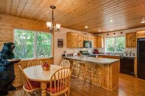 A wooden cabin interior with a dining table, chairs, a kitchen area with wooden cabinets, a refrigerator, and a bear figurine. - Icicle River Cabin w/ Hot Tub + Deck (Leavenworth)