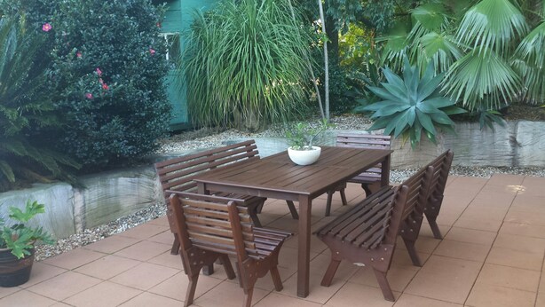Una mesa de madera con seis sillas, rodeada de plantas diversas y un pequeño estanque.