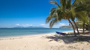 Una playa con una hamaca, un bote azul y palmeras.