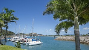 Un puerto deportivo con barcos amarrados, cielo despejado y una zona verde con palmeras.