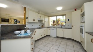 Cozinha com armários brancos, máquina de lavar louça, micro-ondas e janela com vista para plantas.