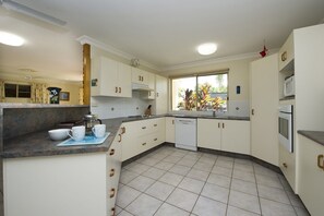 A kitchen with white cabinets, a dishwasher, a microwave, and a window with a view of plants.