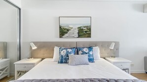 A bedroom with a large bed, two bedside tables, a headboard, and a framed picture on the wall. - Blue on Blue Studio Room 1242 (Nelly Bay)