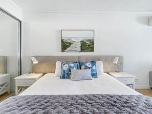 A bedroom with a large bed, two bedside tables, a headboard, and a framed picture on the wall.