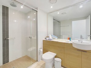 A modern bathroom with a glass shower enclosure, a white toilet, a sink with a mirror, and a wooden vanity.