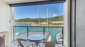 A balcony with a table and chairs, a view of a marina with boats, and a clear sky. - Blue on Blue Studio Room 1242 (Nelly Bay)