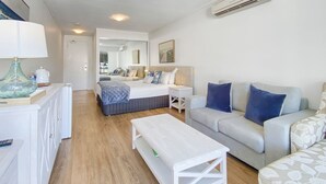 A modern hotel room with a bed, a sofa, a small table, a desk, and a mirror. - Blue on Blue Studio Room 1242 (Nelly Bay)