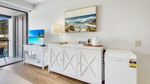 A modern room with a white cabinet, a small table with a lamp, and a refrigerator. - Blue on Blue Studio Room 1242 (Nelly Bay)