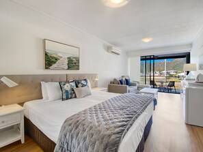 A modern hotel room with a large bed, a desk, a chair, and a view of the outdoors.