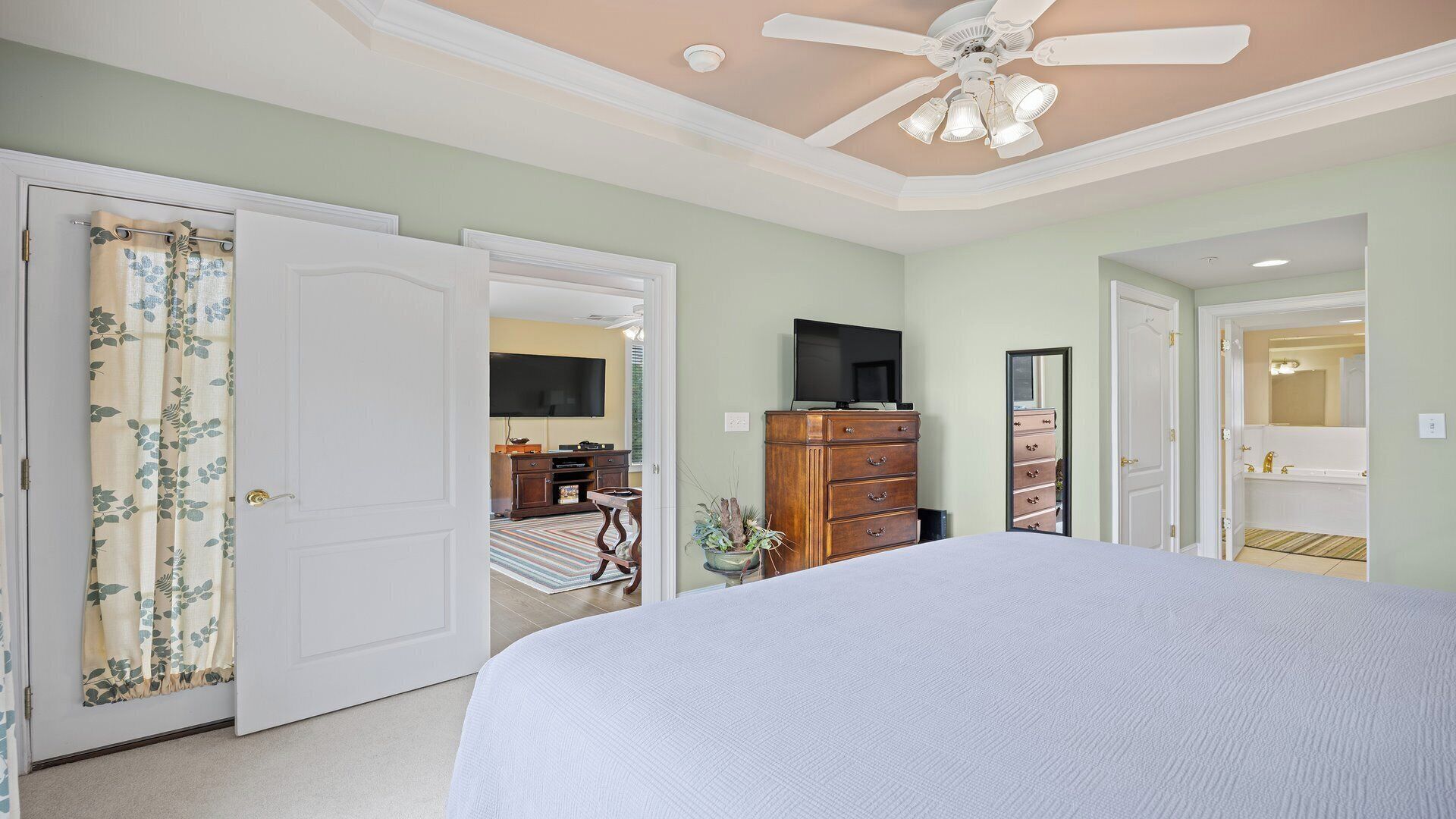 Une chambre à coucher avec un lit, un ventilateur de plafond, une télévision et une commode.