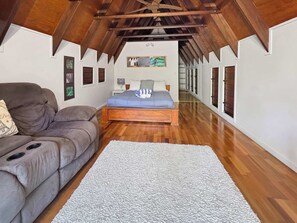 A bedroom with a wooden ceiling, a bed with a blue bedspread, a grey sofa, and a white rug.