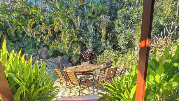 A wooden deck with a red floor leading to a table and chairs, surrounded by lush greenery. - Serene Place (Nelly Bay)