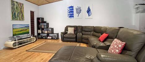 A living room with a sectional sofa, a flat-screen TV, a bookshelf, and artwork on the walls.
