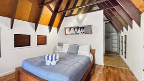 A bedroom with a wooden bed, a bedside table, a lamp, and a large mirror on the wall. - Serene Place (Nelly Bay)