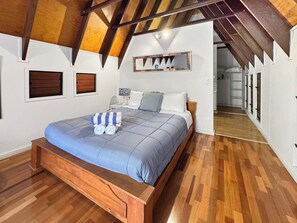A bedroom with a wooden bed, a bedside table, a lamp, and a large mirror on the wall. - Serene Place (Nelly Bay)