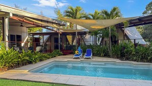 A swimming pool with two lounge chairs, surrounded by greenery and a covered patio area. - Serene Place (Nelly Bay)