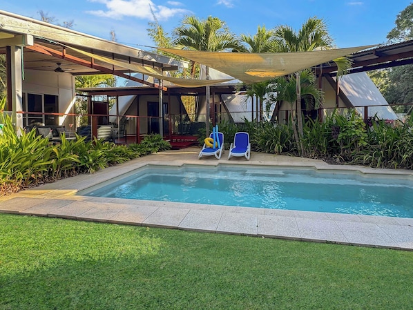 A swimming pool with two lounge chairs, surrounded by greenery and a covered patio area. - Serene Place (Nelly Bay)
