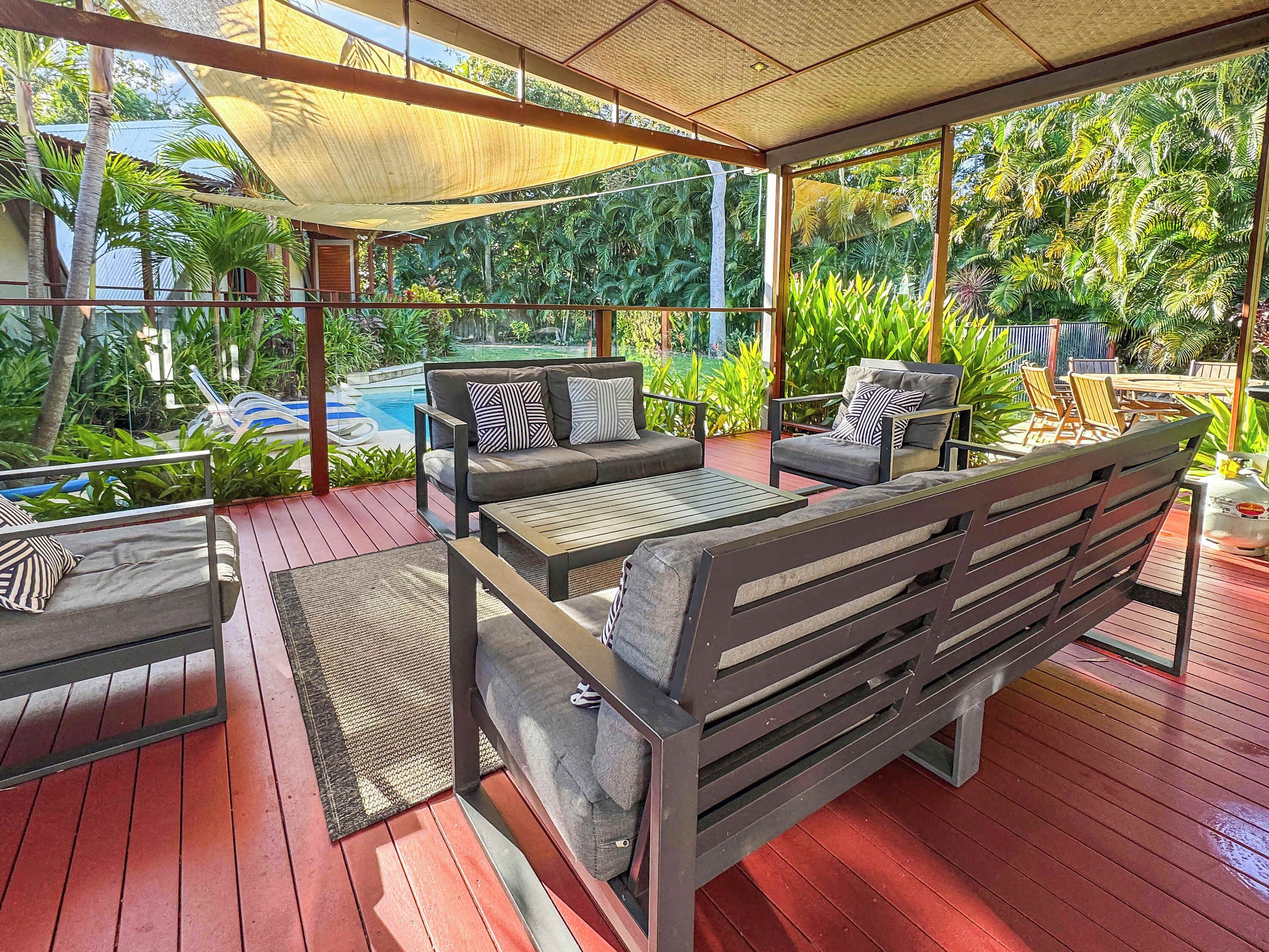 Un espacio de estar al aire libre con piscina, terraza de madera y plantas tropicales.
