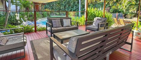 Un espacio de estar al aire libre con piscina, terraza de madera y plantas tropicales.