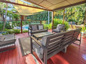 An outdoor seating area with a pool, wooden deck, and tropical plants. - Serene Place (Nelly Bay)