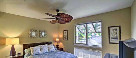 Un dormitorio con cama, lámparas de noche, ventilador de techo, televisión y ventana con persianas.
