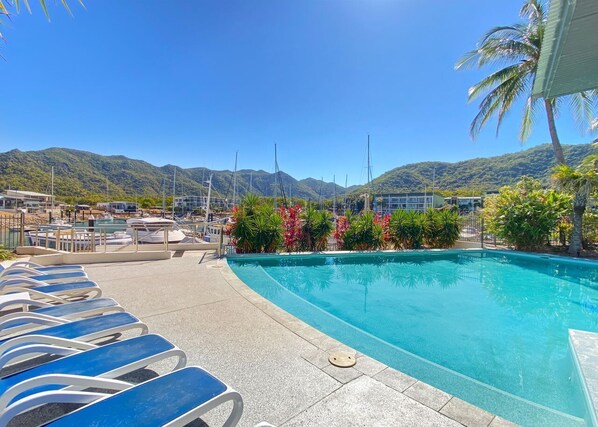 A swimming pool with lounge chairs, surrounded by tropical plants and mountains in the background.